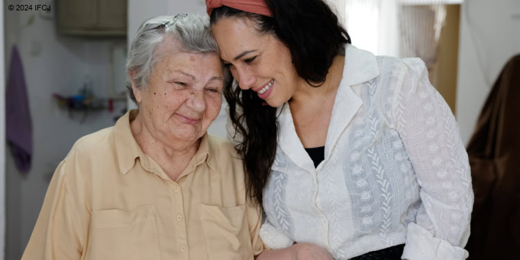 Elderly beneficiary and Yael hold hands.