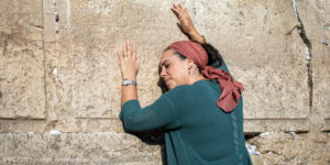 Yael Eckstein, wearing a red scarf over her head, leans against the Western Wall in prayer.